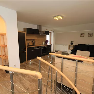 A modern living room with an open kitchen and a cozy sofa. The space is bright and inviting, with functional furniture and a pleasant atmosphere.