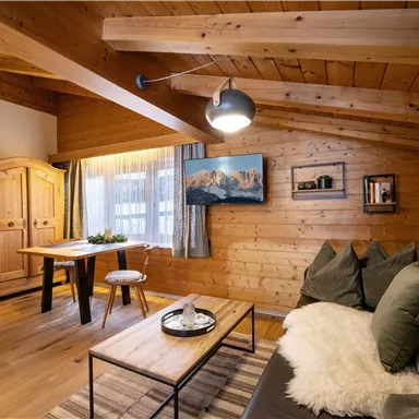 A cozy room with wooden paneling, a modern sofa, and a table. Generous windows provide ample light and an inviting atmosphere.