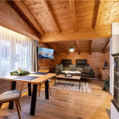 Cozy living room with wooden ceilings and walls. A dining table and a couch create an inviting atmosphere.