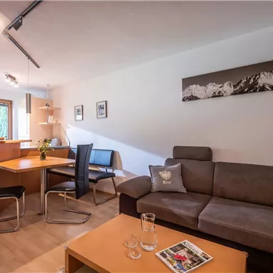 A modern living room with a comfortable sofa and a dining table. Large windows provide bright light and a pleasant atmosphere.