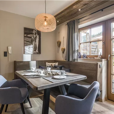 An inviting dining area with a wooden table and cozy chairs. Large windows provide a view outside and let in plenty of daylight.