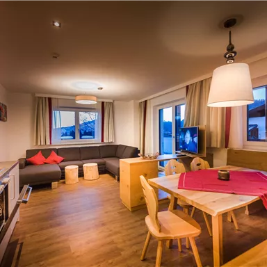 Ein modernes Wohnzimmer mit einer gemütlichen Sitzecke, einem Essbereich und großen Fenstern. Der Raum ist hell und freundlich gestaltet.