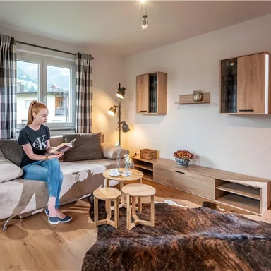A cozy apartment with a bright living room. A woman is sitting on the sofa and reading a book.
