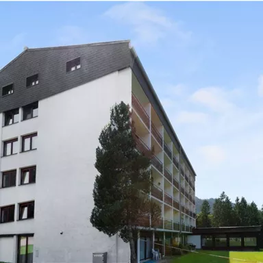 Ein modernes Gebäude mit mehreren Etagen und großen Fenstern. Umgeben von einer grünen Wiese und Bäumen.