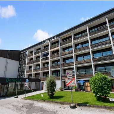 Ein modernes Hotelgebäude mit mehreren Etagen und großen Fenstern. Vor dem Gebäude befindet sich eine gepflegte Grünfläche.