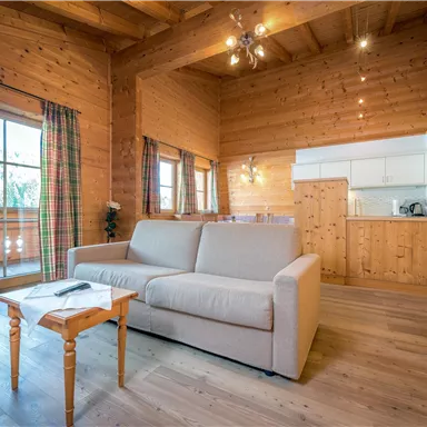 A cozy living space with wood paneling and large windows. In the foreground, there is a bright sofa and a small table.