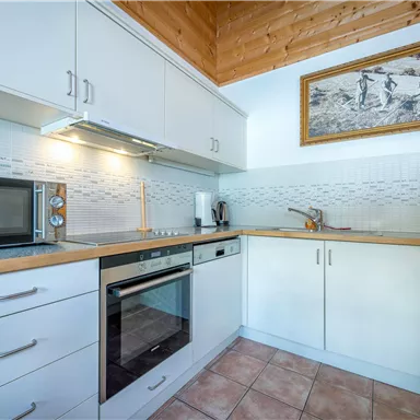 A modern kitchen with white cabinets and wood details. It is equipped with a microwave and an oven.