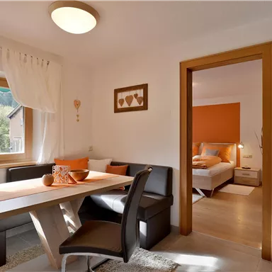 Ein gemütlicher Wohnraum mit einem Essbereich und einem angrenzenden Schlafzimmer. Helle Farben und viel Tageslicht schaffen eine einladende Atmosphäre.