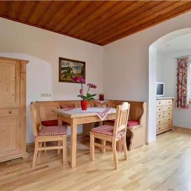 Ein gemütlicher Essbereich mit einem Tisch und Holzstühlen. Im Hintergrund befinden sich ein Sideboard und ein Fenster mit Blick nach draußen.
