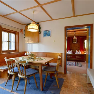 A cozy dining area with a wooden table and chairs. In the background, another room is visible, appearing inviting.