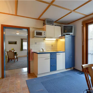 A bright kitchen with blue cabinets and modern appliances. In the background, there is a dining area with a table and chairs.