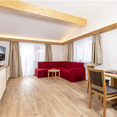 A modern apartment with a wooden ceiling and large windows. It features a cozy seating area, a dining table, and a kitchenette.