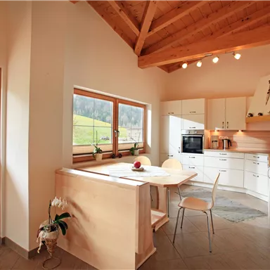 Bright kitchen with modern white furniture and a wood stove. Large windows provide a view of the green meadow outside.