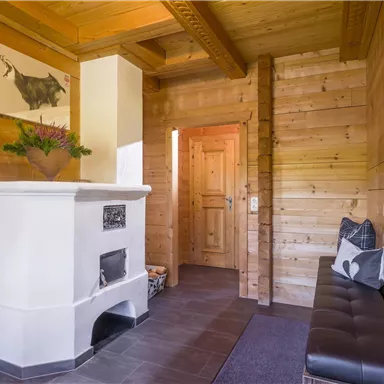 Ein gemütlicher Eingangsbereich mit Holzverkleidung. Ein weißer Ofen und eine Sitzbank verleihen dem Raum eine warme Atmosphäre.