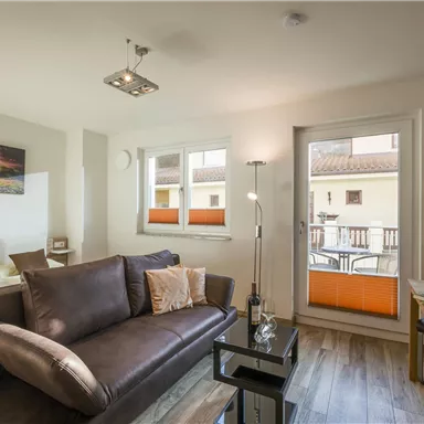 A modern living room with a comfortable sofa and large windows. The room is bright and inviting, with access to a balcony.