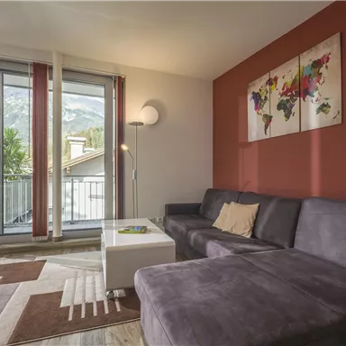 A modern living room with a gray sofa and a white table.
Large windows offer a view of the mountains and the balcony.