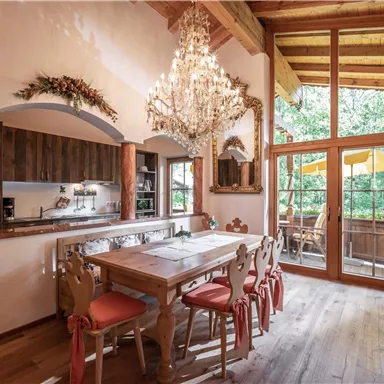 Ein elegantes Esszimmer mit einem großen Holztisch und stilvollen Stühlen. Große Fenster bieten Blick auf eine grüne Umgebung und viel Tageslicht.