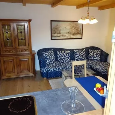A cozy living room setup with a blue sofa and a wooden cabinet. On the table are fruits and a glass vase.