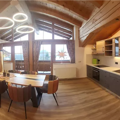 Eine moderne Küche mit offenem Wohnbereich und großen Fenstern. Helle Holzverkleidungen und eine gemütliche Essgruppe schaffen eine einladende Atmosphäre.