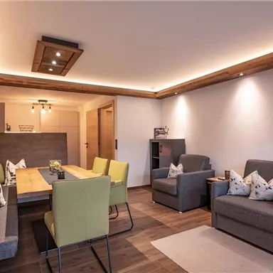 Ein modernes Wohnzimmer mit einem großen Essbereich. Die Einrichtung ist gemütlich und stilvoll, mit einer Mischung aus grauen und grünen Möbeln.