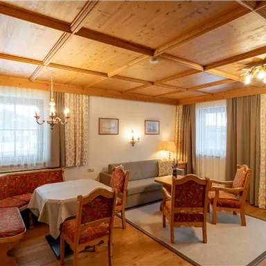 A cozy living space with a wooden table and several chairs. The walls are paneled with wood, and large windows provide plenty of light.