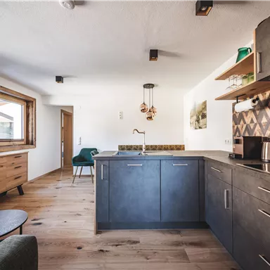 Eine moderne Küche mit einem Holzfußboden und eleganten Möbeln. Die Wände sind hell und es gibt ein großes Fenster, das viel Licht hereinlässt.