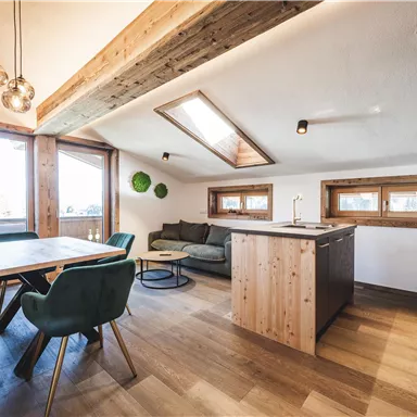 Eine moderne, helle Wohnung mit Holzdetails. Der offene Wohn- und Essbereich ist gemütlich mit einem Tisch und einem Sofa eingerichtet.