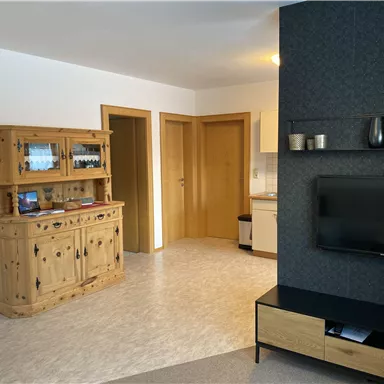 A cozy living space with a wooden cabinet and a television. Bright walls and two doors leading to other rooms can be seen.