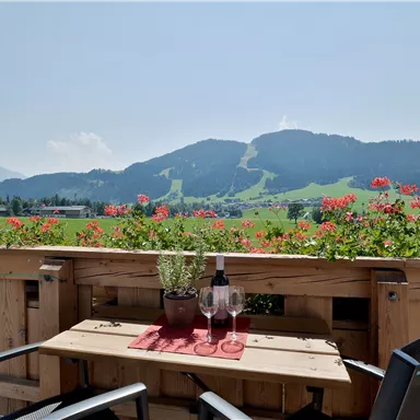 A beautiful view from a terrace over green meadows and mountains. On the table are two glasses and a bottle of wine.