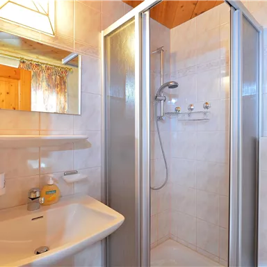 A bright bathroom with a shower cabin and a sink. The walls are tiled and there is a large mirror.