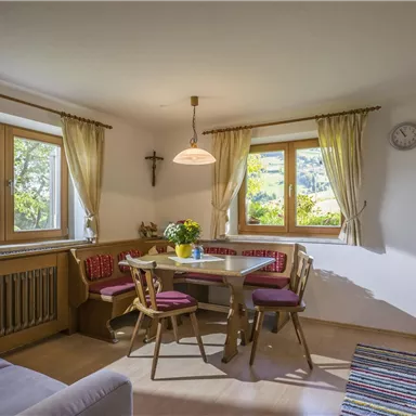 A cozy kitchen with a round table and chairs. Light floods the room through the large windows.