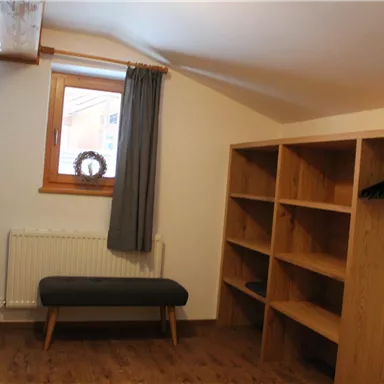 A cozy room with a window, a small wooden sofa, and shelves. The floor is wooden, and the room is bright and inviting.