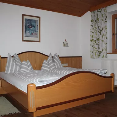 A cozy bedroom with a double bed and light wood. The walls are decorated with floral curtains and a piece of art.