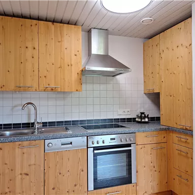 A modern kitchen with wooden furniture and stainless steel appliances. The walls are painted in light tones, and there is a stylish extractor hood.