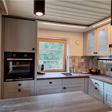 A modern kitchen with wood and tile accents. It features a large window and is well-structured, ideal for cooking.