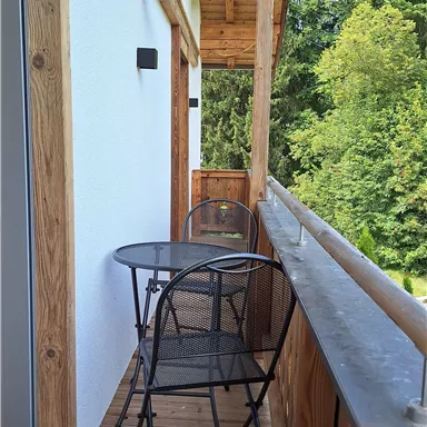 A cozy balcony with a round table and two black chairs. In the background, green trees can be seen.