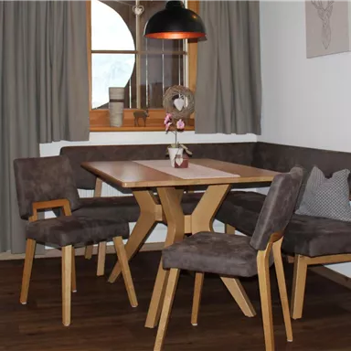 A cozy living area with a dining space, a wooden table, and comfortable chairs. Large windows offer a view of the surroundings and allow for natural light.