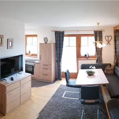 A cozy living space with wooden paneling, a dining table, and a couch. The room has large windows that let in plenty of light.