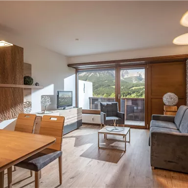 Moderne Wohnung mit einem gemütlichen Wohnzimmer und einer schönen Aussicht auf die Berge. Der Raum ist hell und einladend, mit einem Essbereich und elegantem Mobiliar.