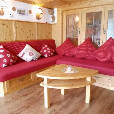 Ein gemütlicher Wohnbereich mit einer roten Polsterbank und bunten Kissen. Der Raum ist aus hellem Holz und hat einen rustikalen Charme.