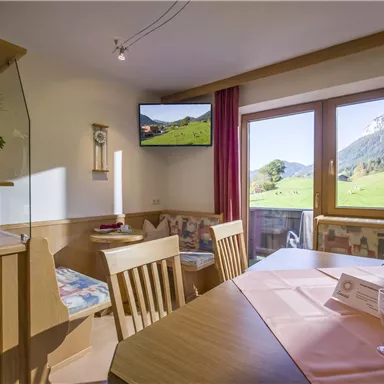 Eine gemütliche Wohnung mit einem Essbereich und großen Fenstern, die einen Blick auf die grüne Landschaft bieten. Ein Fernseher und dekorative Elemente sorgen für eine einladende Atmosphäre.
