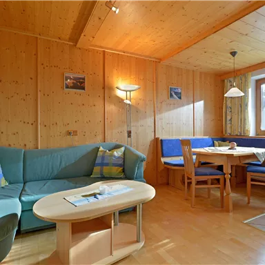 A cozy living room with wood paneling, a blue sofa, and a dining table. Large windows provide plenty of daylight.