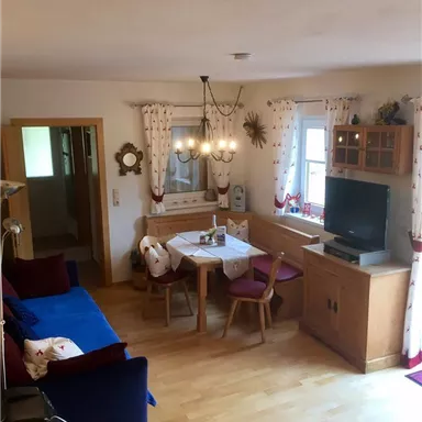 Ein gemütliches Wohnzimmer mit einem blauen Sofa und einem Essbereich. Helle Wände und dekorative Vorhänge schaffen eine einladende Atmosphäre.