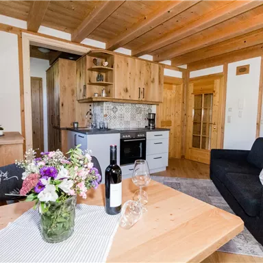 Eine gemütliche Wohnküche mit Holzdekor, einer modernen Küche und einem großen Fenster. Auf dem Tisch steht eine Vase mit Blumen und eine Flasche Wein.