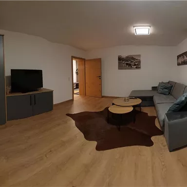 Ein modernes Wohnzimmer mit einem grauen Sofa und einem Couchtisch. Der Raum hat Holzfußboden und neutrale Wände, mit Kunst an der Wand.
