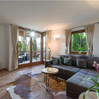 Ein gemütliches Wohnzimmer mit einem grauen Sofa und einem kleinen Tisch. Große Fenster lassen viel Licht herein und bieten einen Blick auf den Balkon.