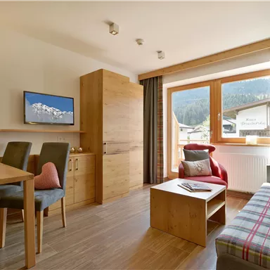 A cozy living room with a dining area and a television. Large windows provide a view of the mountains.