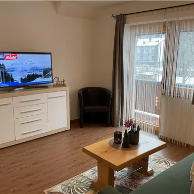 A modern living room with a TV, sofa, and a coffee table. Large windows provide plenty of natural light.
