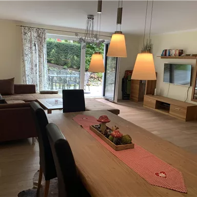 A modern living room with a cozy couch and a dining table. Large windows bring in plenty of light and offer a view of the garden.