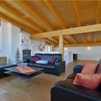 A modern living room with wooden ceilings and large windows. Black sofas and a stylish coffee table arrangement create an inviting atmosphere.